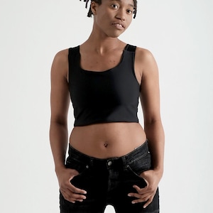 May include: A black cropped vest top with a square neckline and wide shoulder straps, worn with black distressed denim jeans featuring heavy rips and frayed detailing on the legs. The outfit consists of a solid black sleeveless top and jeans.