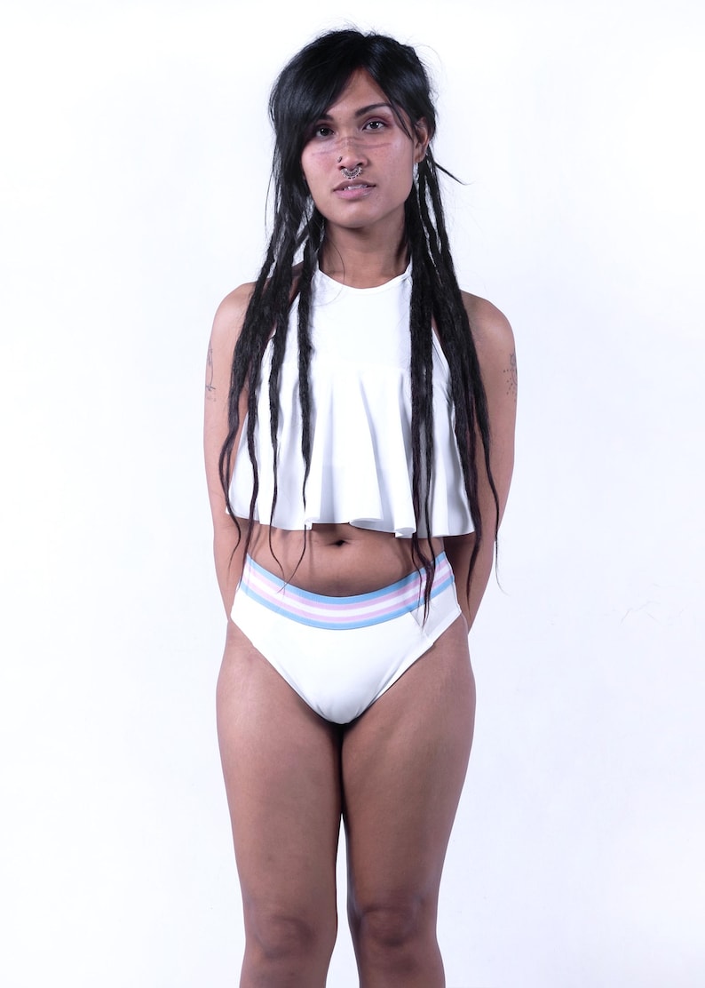 May include: A white two-piece swimsuit. The top is a halter style with a ruffled hem. The high-waisted bottoms feature horizontal stripes in pastel blue, pink, and lavender. The swimsuit is made of a smooth, opaque fabric.