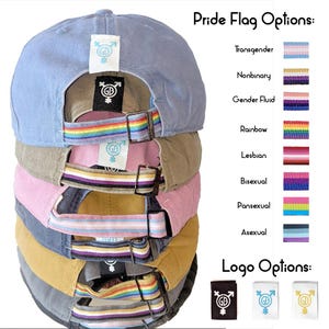 Puede incluir: Pila de seis gorras de béisbol con bandas de banderas del orgullo de diferentes colores. Cada gorra tiene un logotipo de género neutro con las letras "GB" y un símbolo. Las opciones de banderas del orgullo son: Transgénero, No binario, Fluido de género, Arcoíris, Lesbiana, Bisexual, Pansexual, Asexual. Las opciones de logotipo son: negro, blanco y amarillo.