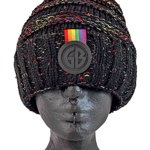 Könnte beinhalten: Schwarze Mütze mit einem Regenbogenstreifen und einem schwarzen Gummilogo mit der Aufschrift "GB".