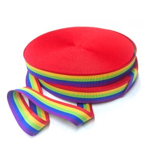 Peut inclure: Ruban rayé arc-en-ciel avec des rayures rouges, orange, jaunes, vertes, bleues et violettes. Le ruban est enroulé et une longueur pend.