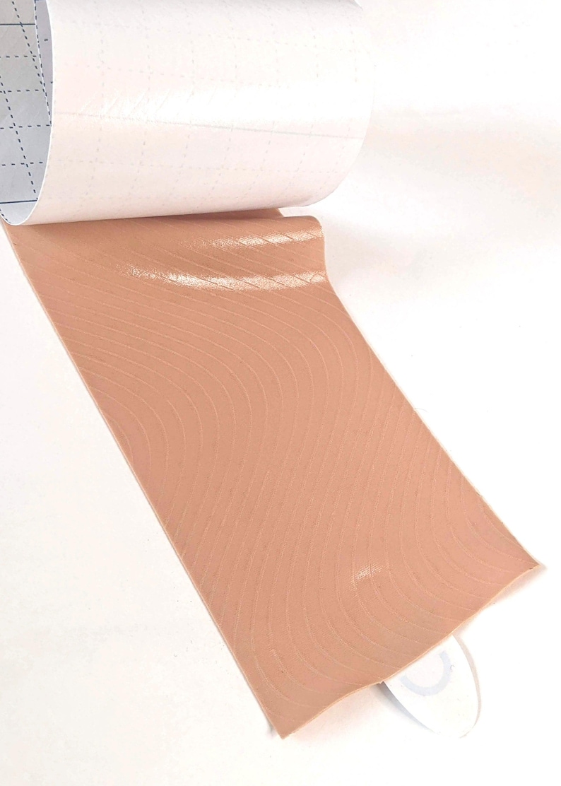 K&ouml;nnte beinhalten: Eine Rolle Klebeband mit einer hautfarbenen, strukturierten Oberfl&auml;che. Das Band ist so konzipiert, dass es wie menschliche Haut aussieht.