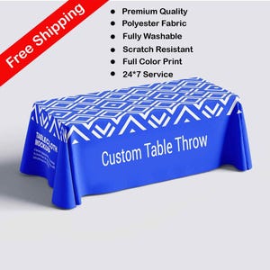 Può includere: Una tovaglia blu personalizzata con motivi geometrici bianchi. Il testo "Custom Table Throw" è visualizzato sul davanti. Il testo aggiuntivo include "Premium Quality", "Polyester Fabric", "Fully Washable", "Scratch Resistant", "Full Color Print" e "24*7 Service".