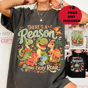 Könnte beinhalten: Dunkelgraues T-Shirt mit einem farbenfrohen Dinosaurier-Motiv und dem Text "There's a Reason Behind Every Roar". Das Design zeigt verschiedene Dinosaurier in Grün-, Orange- und Blautönen. Zusätzliche Shirts mit dem gleichen Design sind ebenfalls abgebildet.