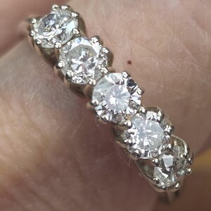 May include: A silver ring featuring five round, clear gemstones. The gemstones are set in individual, ornate settings, creating a sparkling, elegant design. The ring is likely made of silver or a similar metal.