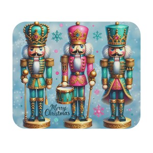 Puede incluir: Tres cascanueces decorativos en verde azulado, rosa y dorado, cada uno con un diseño único. Los cascanueces están sobre bases decorativas, con las palabras "Merry Christmas" en el centro. El fondo es azul claro con copos de nieve.