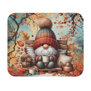 May include: A whimsical illustration of a gnome seated on a wooden bench, holding a mug of coffee. The gnome wears a red and gray knit hat with a pom-pom. Autumn leaves and a teapot surround the gnome, creating a cozy fall scene.