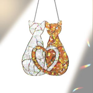 Puede incluir: Un atrapasoles de cristal con dos gatos formando un coraz&oacute;n. Un gato es blanco, el otro naranja y dorado. Cuelga de una cadena plateada. Las medidas est&aacute;n en cm.