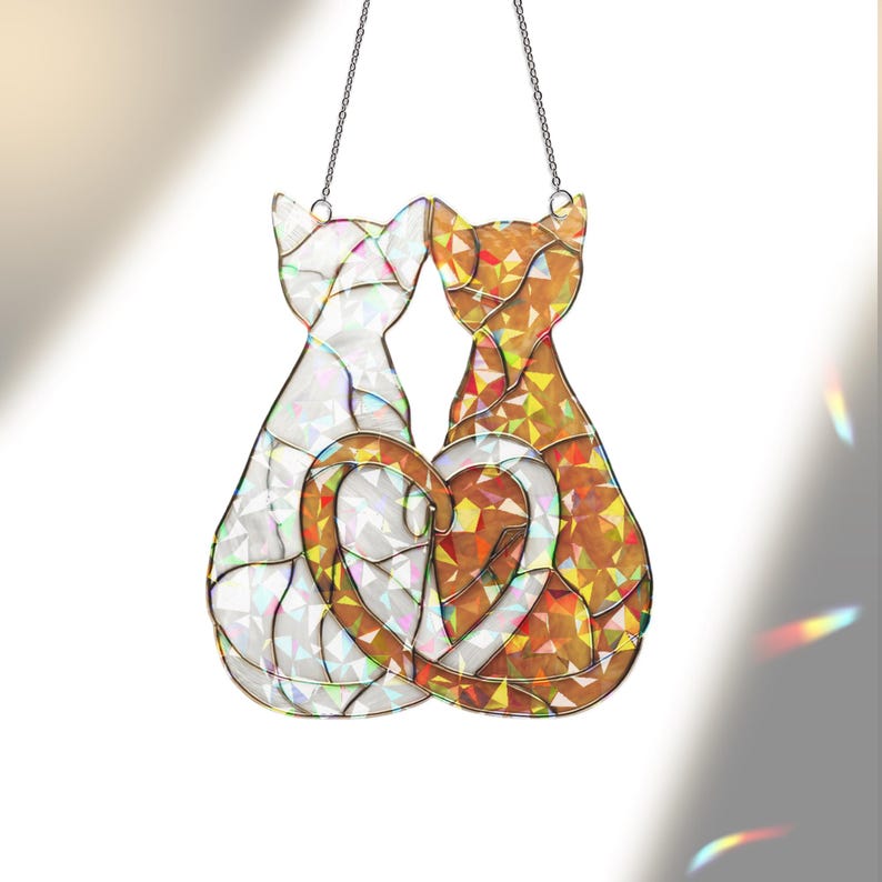 Puede incluir: Un atrapasoles de cristal con dos gatos formando un coraz&oacute;n. Un gato es blanco, el otro naranja y dorado. Cuelga de una cadena plateada. Las medidas est&aacute;n en cm.