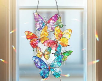 May include: A colorful butterfly suncatcher with a variety of vibrant colors, including red, orange, yellow, green, blue, and purple. The butterflies are arranged in a cluster and are suspended by a silver chain. The suncatcher is hanging in front of a window.