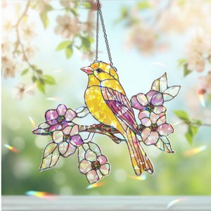 May include: A stained glass suncatcher featuring a yellow bird perched on a branch with pink flowers. The bird has a pink breast and a long tail. The flowers are iridescent and have a pink and purple color scheme.