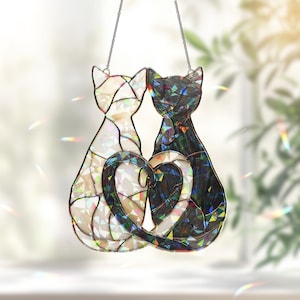 Puede incluir: Atrapasoles de gato de vidriera con dos gatos cuyas colas forman un coraz&oacute;n. Un gato es blanco, el otro negro, ambos con detalles iridiscentes. Los gatos est&aacute;n suspendidos por una cadena plateada.