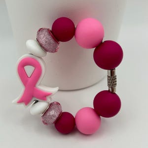 May include: Pink and burgundy beaded bracelet with a pink ribbon charm. The bracelet has a silver clasp.