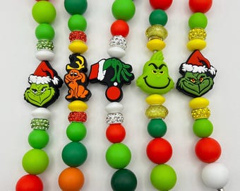 May include: Five Grinch-themed Christmas bead bracelets with different charms, including the Grinch, Max the dog, and a Santa hat. The bracelets are made with green, red, white, and orange beads.
