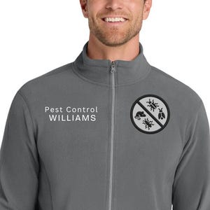 May include: A grey zip-up fleece jacket featuring the text "Pest Control WILLIAMS" in white on the left chest. A circular emblem with a bug symbol is on the right chest. The jacket has a full zip and two side pockets.