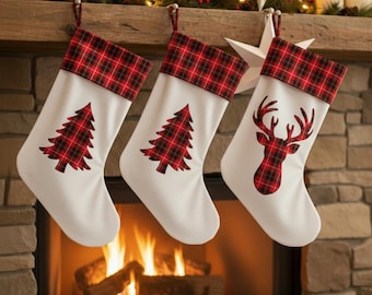 Pode incluir: Três meias de Natal brancas com tops xadrez vermelhos e pretos e designs correspondentes. Duas meias apresentam uma árvore de Natal xadrez vermelha e uma tem uma cabeça de rena xadrez vermelha. Elas penduram acima de uma lareira.