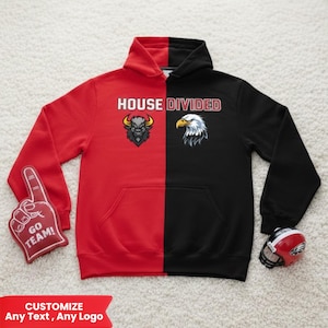 Peut inclure: Un sweat à capuche bicolore rouge et noir avec le texte "HOUSE DIVIDED". Le côté rouge présente un taureau, le côté noir un aigle. Un doigt en mousse rouge avec "GO TEAM!" et un mini casque de football sont également présents.