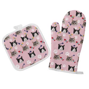 May include: A pink oven mitt and pot holder set with a repeating pattern of cat faces and fish bones.
