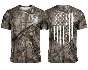 Könnte beinhalten: T-Shirt mit Camouflage-Muster und weißem amerikanischem Flaggen-Design auf Vorder- und Rückseite. Auf der Rückseite des Shirts steht das Wort "FATHER" vertikal in den Streifen der Flagge. Das Shirt hat einen Rundhalsausschnitt und kurze Ärmel.