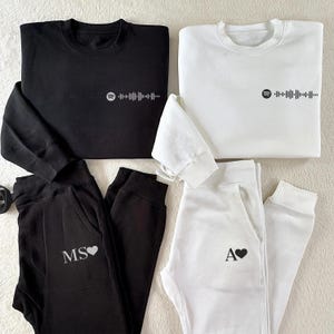 以下が含まれることがあります： 黒と白のジョギングパンツとスウェットシャツの2つのセット。スウェットシャツにはSpotifyのロゴとバーコードが前面に付いています。ジョギングパンツには「MS」と「A」のイニシャルとハートが前面に付いています。