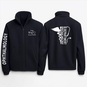 May include: Black fleece zip-up jacket with white text on the sleeves and back. The left sleeve says "OPHTHALMOLOGY". The back says "OPH DEPARTMENT OPHTHALMOLOGY" with a caduceus symbol. The right sleeve says "Erica Physician Assistant" with a heart and EKG symbol.