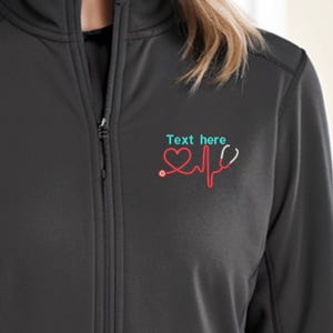 Puede incluir: Chaqueta negra con cremallera con un corazón rojo, un estetoscopio y un gráfico de latido del corazón en el pecho izquierdo. El texto "Text here" está por encima del gráfico.