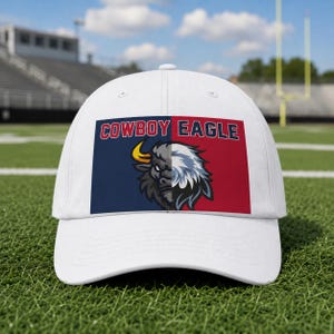 Könnte beinhalten: Eine weiße Baseballkappe mit einer rechteckigen Grafik auf der Vorderseite. Die Grafik ist in eine marineblaue Seite mit einem Bisonkopf und eine rote Seite mit einem Adlerkopf unterteilt. Der Text COWBOY EAGLE ist in Weiß über dem Motiv gedruckt.