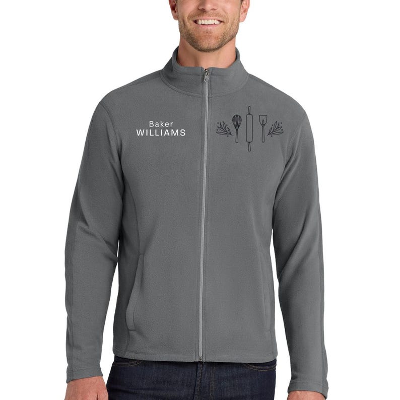 May include: A gray zip-up fleece jacket with the text "Baker WILLIAMS" and a graphic of baking tools. The jacket has a full zipper and two front pockets. The fleece is a solid gray color.