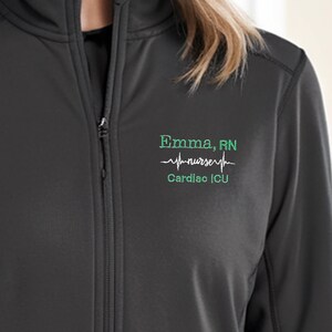 Peut inclure: Veste noire zippée avec un motif brodé vert qui indique "Emma, RN" avec un graphique de battement de cœur et le texte "Cardiac ICU".