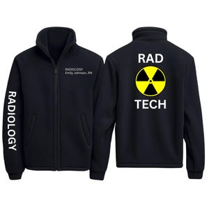 May include: Black fleece jacket with a full zipper and a high collar. The left sleeve has the word "RADIOLOGY" printed vertically in white. The front of the jacket has the text "RADIOLOGY Emily Johnson, RN". The back of the jacket has the words "RAD TECH" with a yellow radiation symbol.