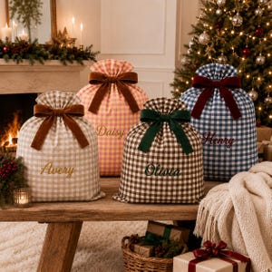 Pode incluir: Quatro sacos de presente em tecido com padrões xadrez vichy em bege, rosa, castanho e azul. Cada saco é fechado com um laço de veludo e bordado com os nomes Avery, Daisy, Olivia e Henry em letra cursiva na parte da frente.