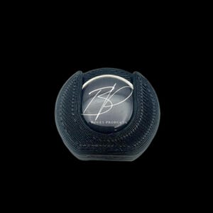 May include: A black, 3D-printed product holder with a circular design. The holder features a central, circular insert with the text "BP" in a stylized script, and the words "ROGEY PRODUCTS" below. The holder is set against a black background.