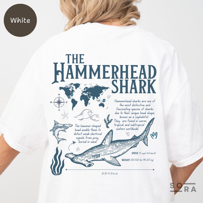 K&ouml;nnte beinhalten: Wei&szlig;es T-Shirt mit einer blauen Grafik eines Hammerhais, einer Weltkarte und dem Text "The Hammerhead Shark". Der Text enth&auml;lt Informationen &uuml;ber die einzigartige Kopfform des Hais, seinen Lebensraum und seine Gr&ouml;&szlig;e. Der Text enth&auml;lt auch die W&ouml;rter "Speed" und "Weight".