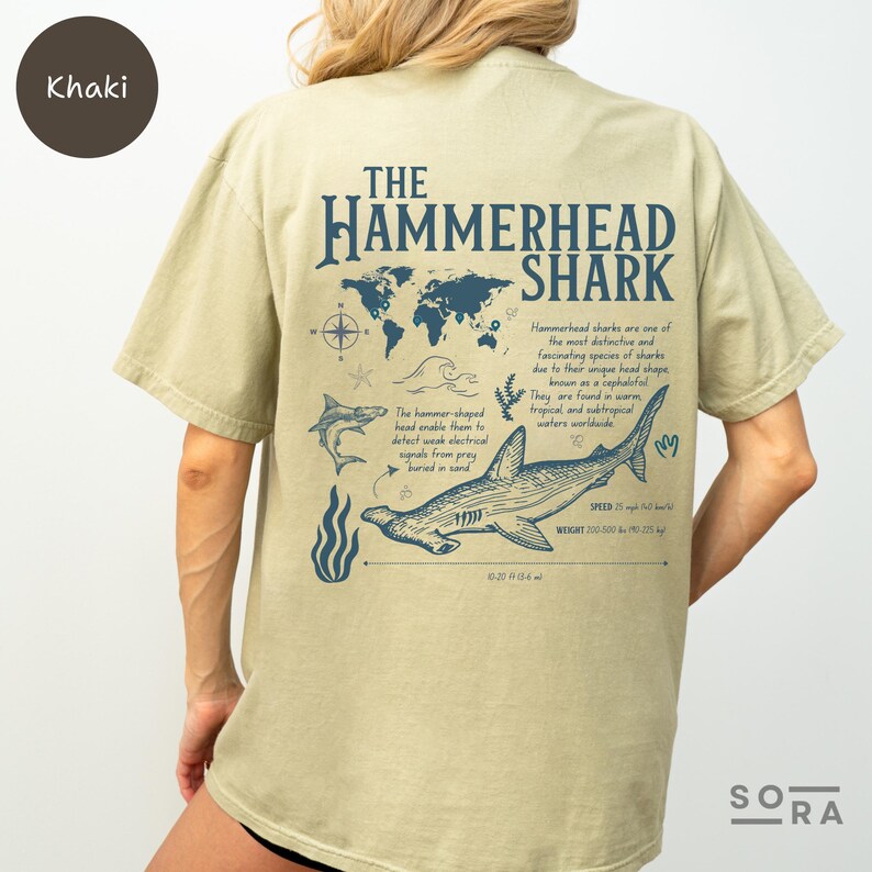 K&ouml;nnte beinhalten: Khaki T-Shirt mit einem Grafikdruck eines Hammerhais und dem Text "THE HAMMERHEAD SHARK". Die Grafik zeigt eine Weltkarte, einen Hammerhai und Informationen &uuml;ber die Geschwindigkeit und das Gewicht des Hais.