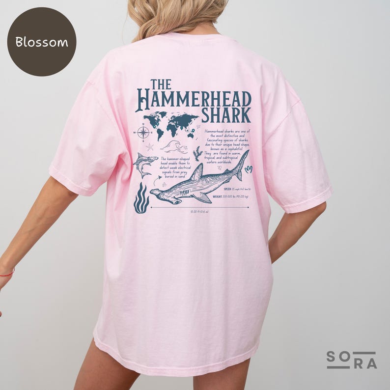 K&ouml;nnte beinhalten: Ein pinkfarbenes T-Shirt mit einem Grafikdruck eines Hammerhais und dem Text "The Hammerhead Shark". Die Grafik enth&auml;lt eine Weltkarte, einen Kompass und Informationen &uuml;ber den Hai.