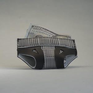 Puede incluir: Una cartera de cuero a cuadros en blanco y negro con forma de pañal con un billete de 100 € que sobresale de la parte superior.