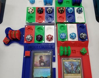 May include: A blue and red 3D printed game organizer with dice, cards, and a command zone. The cards are "The Earthshaker Kiora" and "Alistair, the Brigadier".