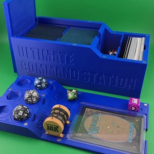 May include: A blue plastic storage box with the words "ULTIMATE COMMAND STATION" printed on the side. The box has compartments for cards, dice, and a life counter. The box is open and the compartments are visible.