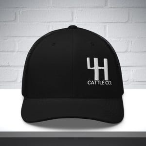 Puede incluir: Gorra de camionero negra con visera curva y parte trasera de malla. La gorra presenta un logotipo bordado en blanco de un "4H" estilizado y el texto "CATTLE CO."