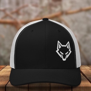 May include: Black and white trucker hat with a wolf head logo. The hat features a black front panel and bill, a white mesh back, and a white embroidered wolf head design on the front.