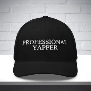 Peut inclure: Casquette de camionneur noire avec du texte brodé blanc qui dit "PROFESSIONAL YAPPER".