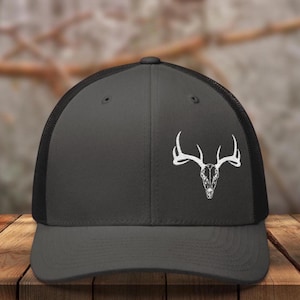 May include: A dark gray and black trucker hat with a white deer skull and antlers graphic.