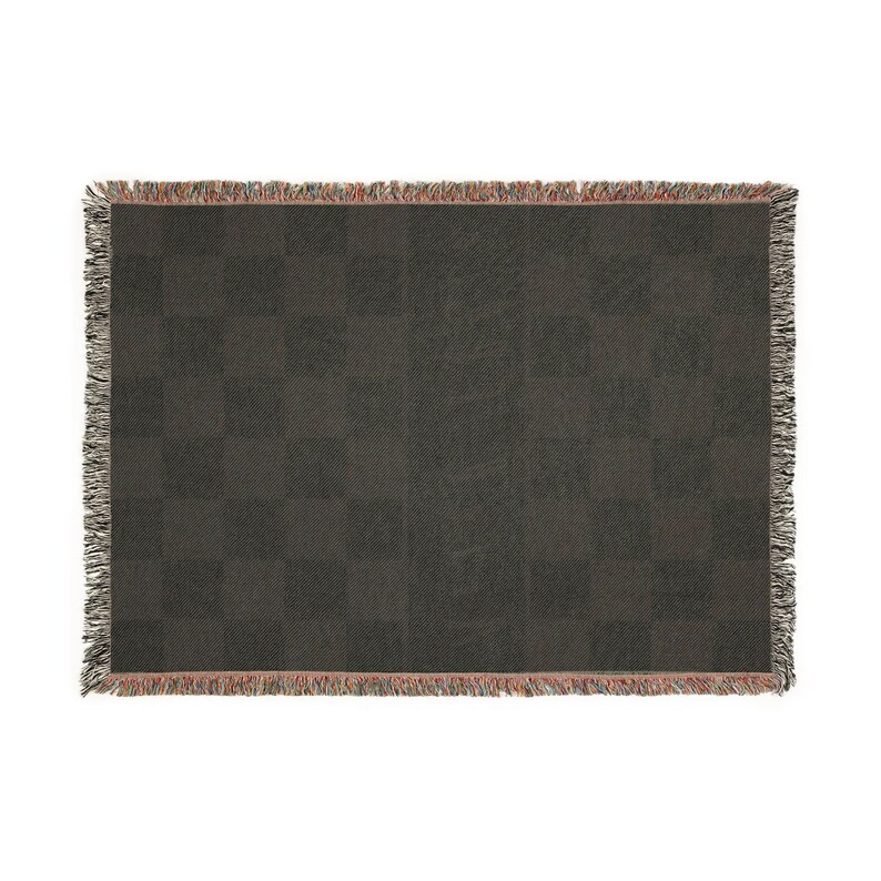 May include: A dark grey woven throw blanket with a chequered pattern. The blanket has a fringed edge with a mix of colours, including red, grey, and white. The blanket is rectangular and appears to be made of a soft material.