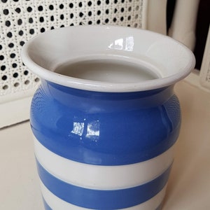 Op de afbeelding: Een keramische vaas met een blauw-wit gestreept patroon. De vaas heeft een brede, uitlopende rand en een cilindrische body. De blauwe strepen wisselen af met witte strepen. De vaas staat op een wit oppervlak. Hoogte ca. 15 cm.