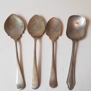 Op de afbeelding: Vier antieke zilveren lepels met verschillende komvormen en handvatontwerpen zijn gerangschikt op een wit oppervlak. De lepels variëren in grootte en stijl en tonen een verzameling vintage zilverwerk.