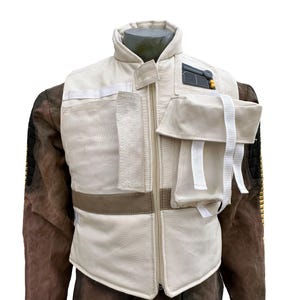 Peut inclure: Un gilet crème avec plusieurs poches et un col montant. Le gilet a une fermeture éclair et une bande marron à la taille. Des sangles blanches et un petit panneau noir et jaune sont visibles sur le gilet.