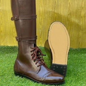 Może przedstawiać: Brązowe skórzane buty jeździeckie ze sznurowaniem z przodu i klamrami. Buty mają spiczasty nosek i grubą podeszwę.