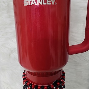 May include: A white ceramic mug with a black handle and the text "But First, Coffee" in a bold, black font. The mug is set against a neutral background, highlighting its simple design.