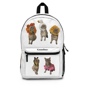 May include: White backpack with five cats in costumes: a sunflower, a duck, a lion, a bee, and a pink tutu. The word "Gumbus" is printed in black on the front. The backpack has a black top handle, a front pocket, and a side mesh pocket.