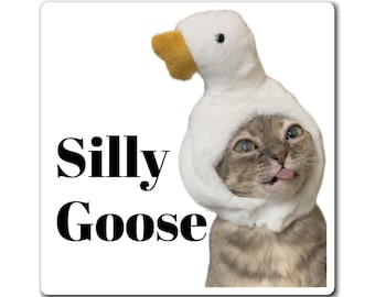 May include: A square sticker featuring a gray tabby cat wearing a white plush goose hat with a yellow beak. The cat has its tongue sticking out. The text "Silly Goose" is printed in a bold black serif font on the left side of the sticker.